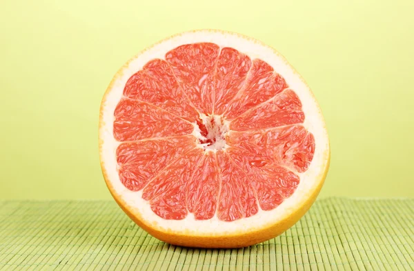 De helft van rijp grapefruit op bamboe mat op groene achtergrond — Stockfoto