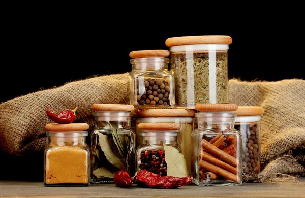 Jars with spices on wooden table on black background — Stock Photo, Image