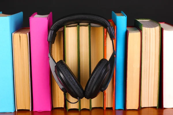 Kopfhörer auf Bücher auf Holztisch auf schwarzem Hintergrund — Stockfoto