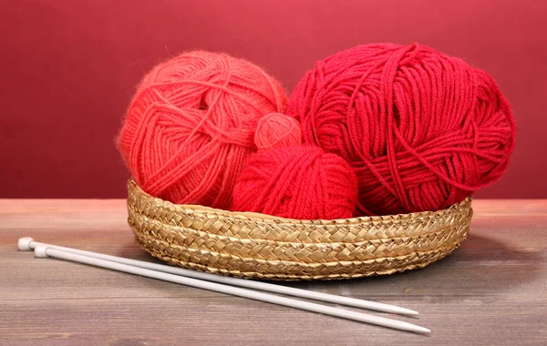 Red knittings yarns in basket on wooden table on red background — Stock Photo, Image