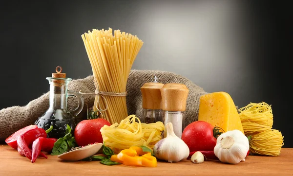 Nudelspaghetti, Gemüse und Gewürze, auf Holztisch, auf grauem Hintergrund — Stockfoto