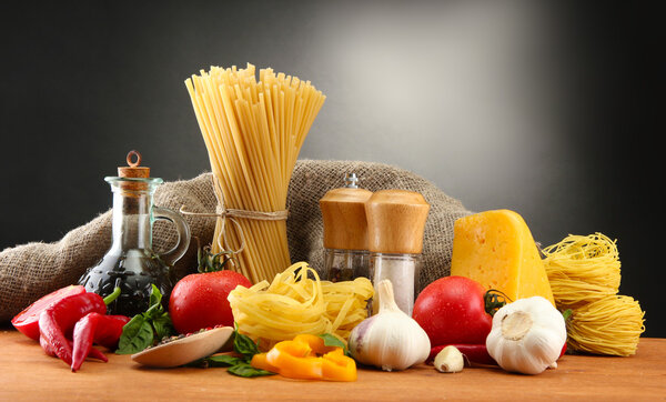 Pasta spaghetti, vegetables and spices, on wooden table, on grey background