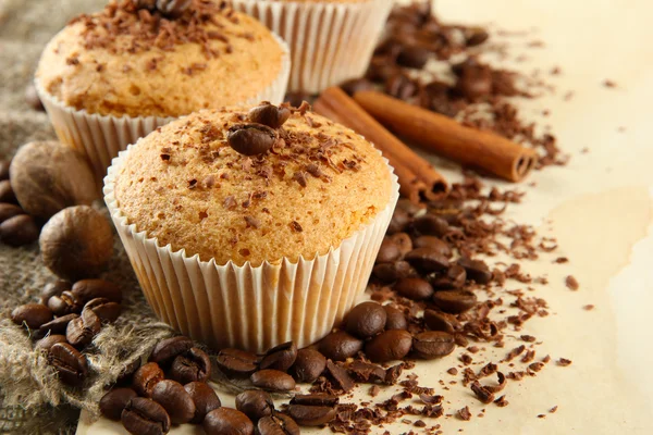 Tasty muffin cakes with chocolate, spices and coffee seeds, on beige background — Stock Photo, Image