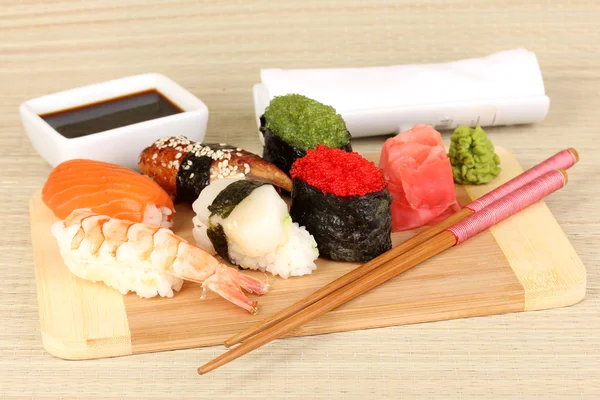 Heerlijke sushi geserveerd op een houten bord op bamboe mat — Stockfoto