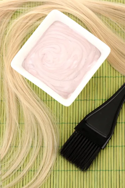 Tinte para el cabello en un tazón y cepillo para la coloración del cabello en una esterilla de bambú verde, primer plano — Foto de Stock