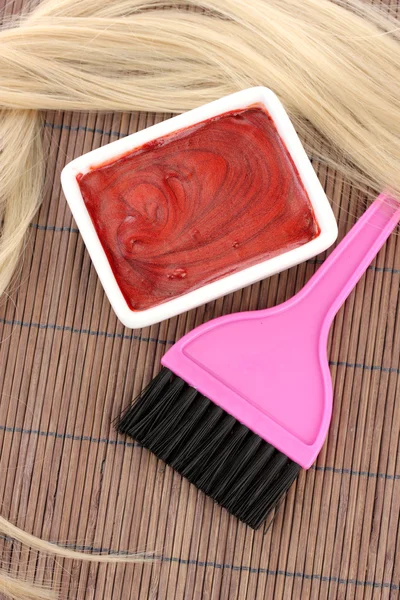 Hair dye in bowl and brush for hair coloring on brown bamboo mat, close-up Stock Image