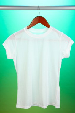 Askı üzerinde yeşil bir arka plan üzerinde beyaz t-shirt