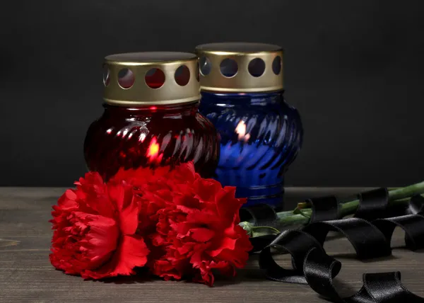 Paměti lucerny se svíčkami, červené karafiáty a hadr na dřevěný stůl na šedém pozadí — Stock fotografie
