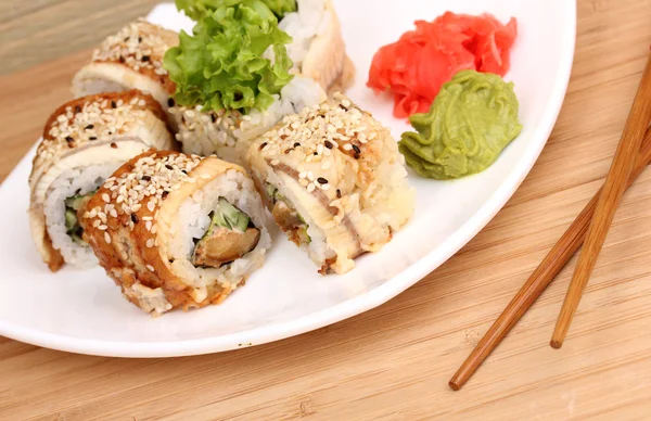 Tasty rolls served on white plate with chopsticks on wooden table close-up — Stock Photo, Image