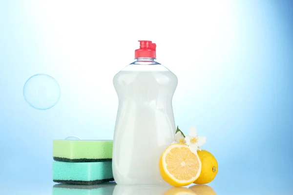 Dishwashing liquid with sponges and lemon with flowers on blue background — Stock Photo, Image