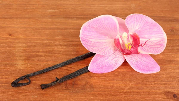 Vanilla pods with flower on wooden background — Stock Photo, Image