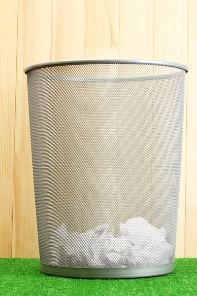 Metal trash bin from paper on grass on wooden background