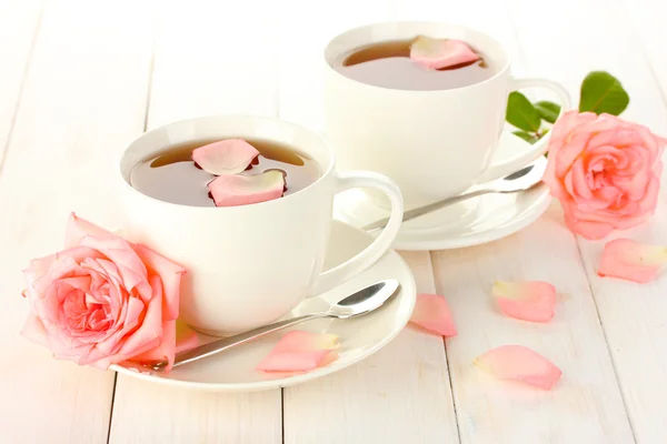 Tassen Tee mit Rosen auf weißem Holztisch — Stockfoto