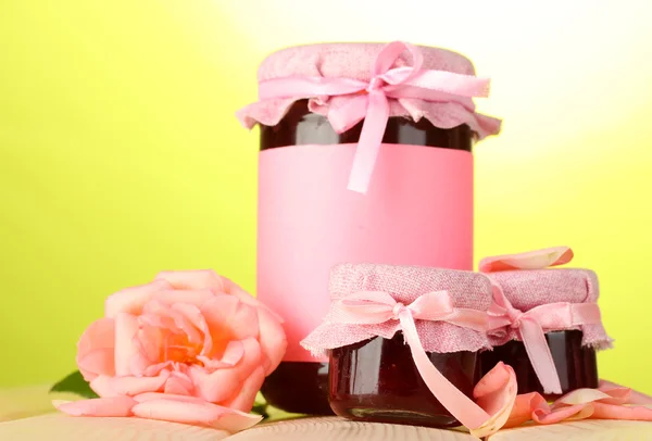 Jars with rose jam and flower on wooden table on green background — Stock Photo, Image