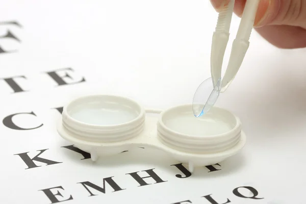 Kontaktlinser i behållare och pincetter, på snellen öga diagram bak — Stockfoto