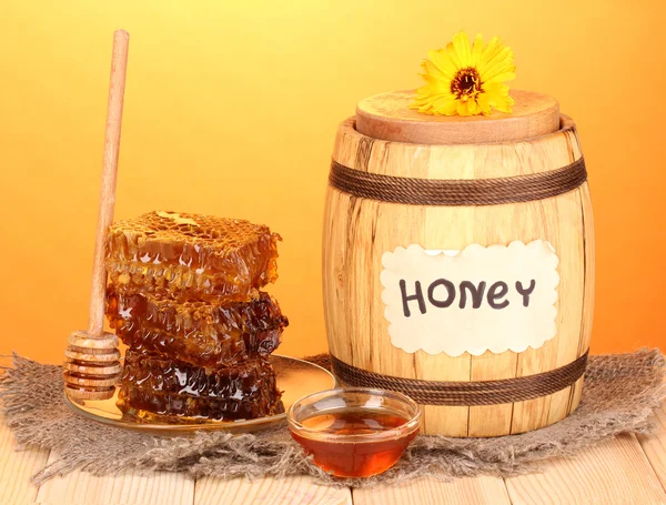 Cañón de miel y panal sobre mesa de madera sobre fondo naranja —  Fotos de Stock