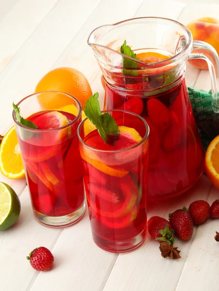 Sangria em jarra e copos com frutas, sobre mesa de madeira branca — Fotografia de Stock