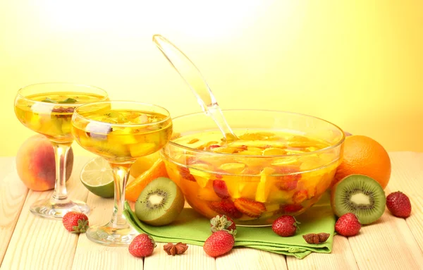 Punch in bowl and glasses with fruits, on wooden table, on yellow backgroun — Stock Photo, Image