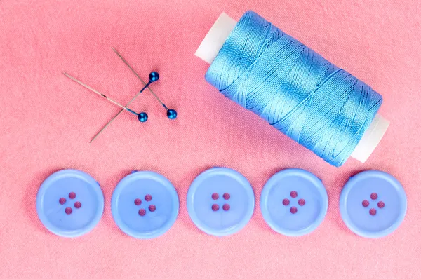 Цветные швейные пуговицы с ниткой на розовой ткани — стоковое фото