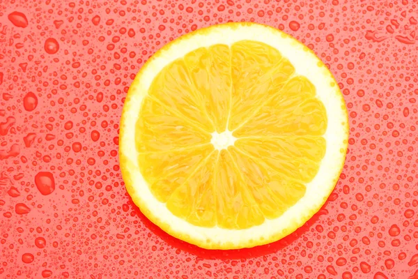 Orangenscheibe mit Tropfen auf rotem Hintergrund — Stockfoto