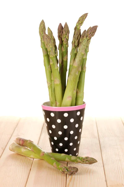 Fresh asparagus in colorful pot on wooden table on white background — Stock Photo, Image