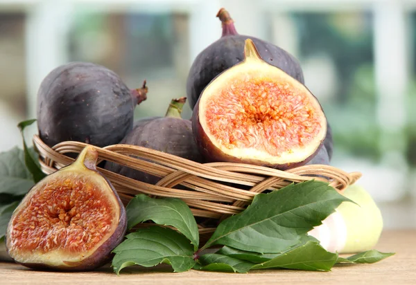 Ripe sweet figs with leaves in basket, on wooden table, on window backgroun