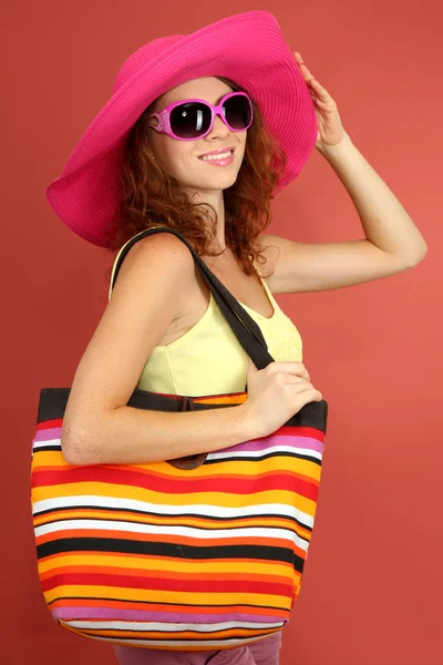 Hermosa chica sonriente con sombrero de playa, gafas y bolso de playa en rosa backgr —  Fotos de Stock