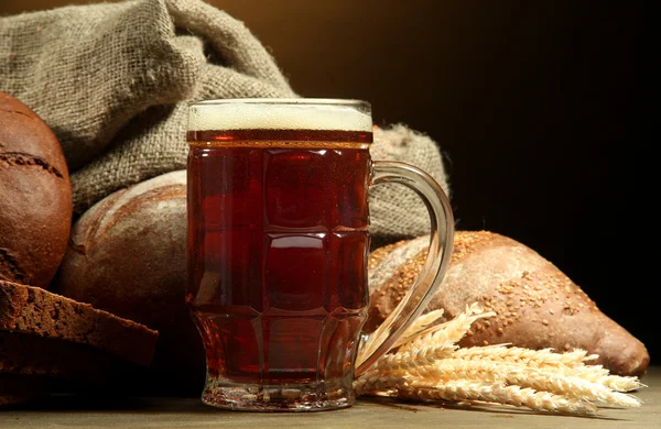 Tankard of kvass and rye breads with ears, on wooden table on brown backgro — Stock Photo, Image