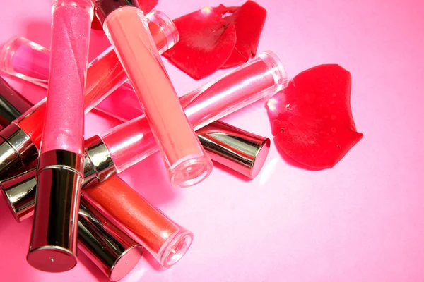 Beautiful lip glosses with rose petals, on pink background — Stock Photo, Image
