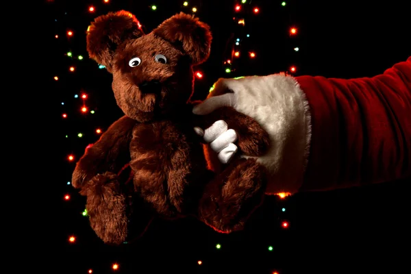 산타 클로스 손을 밝은 배경에 장난감 곰 잡고 — 스톡 사진