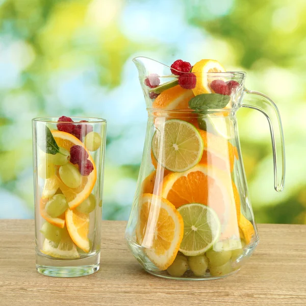 Jar and glass with citrus fruits and raspberries, on green background — Stock Photo, Image