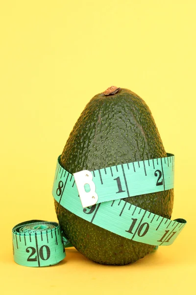 Avocado with measuring tape on yellow background — Stock Photo, Image