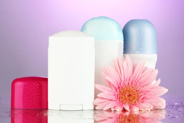 Deodorant botttles met bloem op paarse achtergrond — Stockfoto