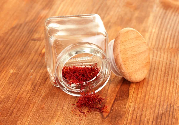 Stigmas of the saffron poured out a glass jar on wooden background close-up — Stock Photo, Image