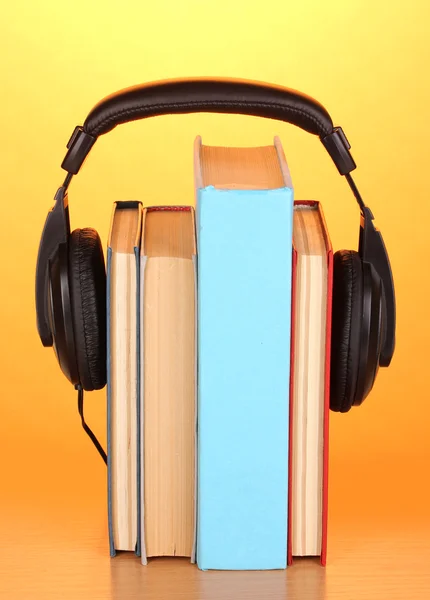 Koptelefoon op boeken over houten tafel op oranje achtergrond — Stockfoto