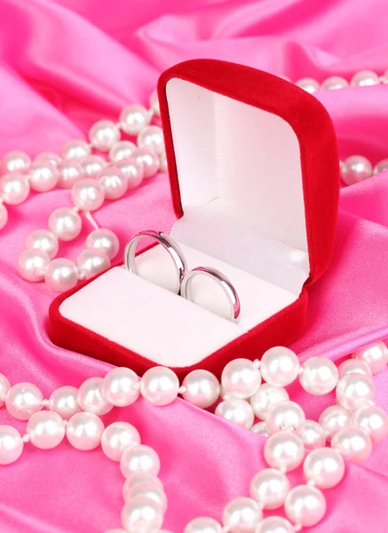 Anillos de boda en caja roja sobre fondo de tela rosa —  Fotos de Stock