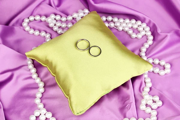 Anillos de boda en almohada de satén sobre fondo de tela púrpura — Foto de Stock