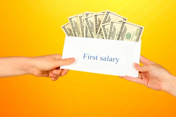 Woman's hand passes the envelope with the salary on yellow background