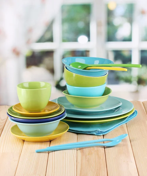 Colorful tableware on wooden table on window background — Stock Photo, Image