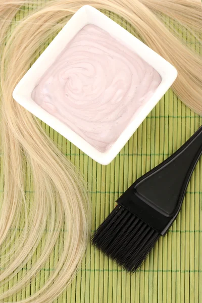 Tintura de cabelo na tigela e escova para coloração de cabelo no tapete de bambu verde, close-up — Fotografia de Stock