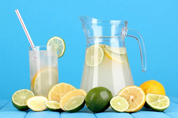 Zitruslimonade im Krug und ein Glas Zitrusfrüchte auf einem Holztisch auf blauem Hintergrund — Stockfoto