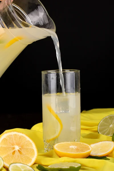 Цитрусовый лимонад в стекле и кувшин цитрусовых вокруг на желтой ткани на деревянном столе крупным планом — стоковое фото