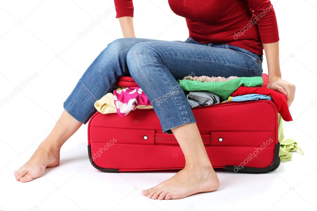 The girl is trying to close suitcase crammed on white background