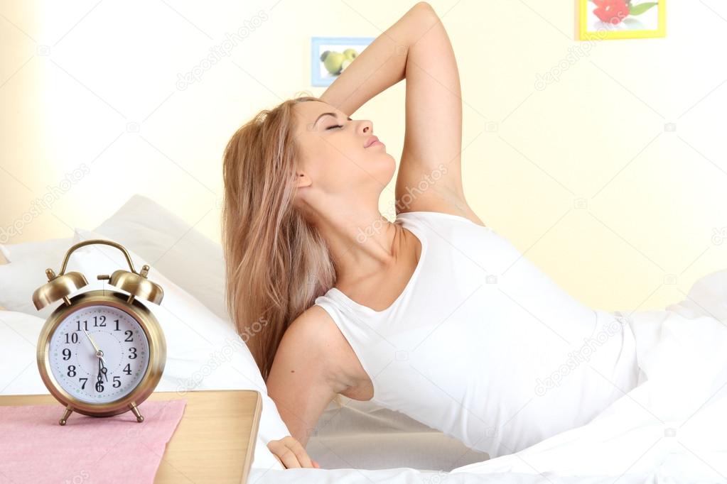 young beautiful woman lying on bed with alarm clock in bedroom