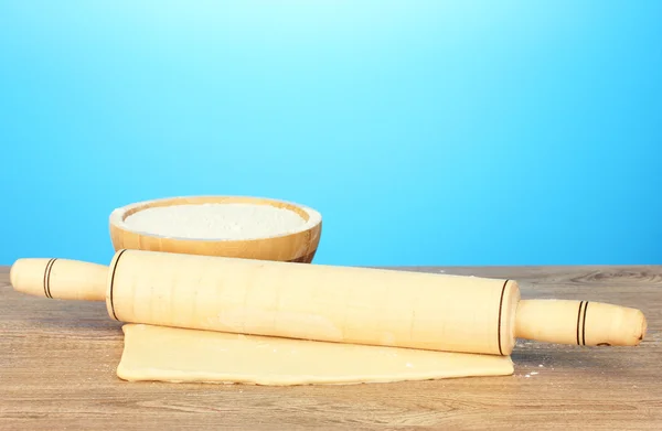 The dough with a rolling pin on wooden table on blue background — Stock Photo, Image