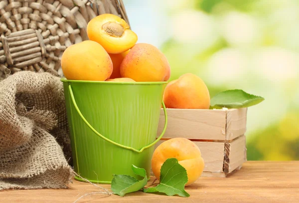 Seau et boîte en bois avec abricots mûrs sur table en bois sur fond vert — Photo