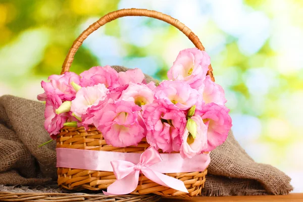 Bouquet of eustoma flowers in basket, on wooden table, on green background — Stock Photo, Image