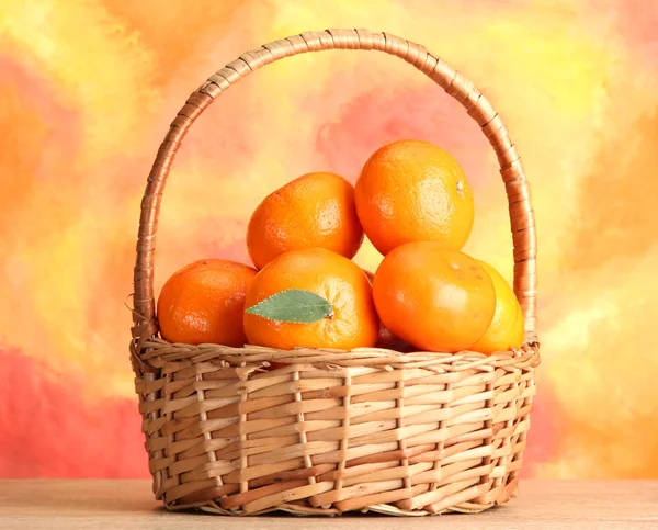 Tangerines with leaves in a beautiful basket, on wooden table on orange background — Stock Photo, Image