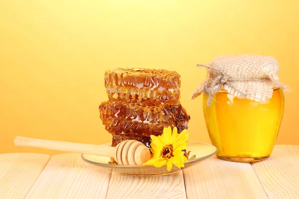 Jar of honey and honeycomb on wooden table on orange background — Stock Photo, Image