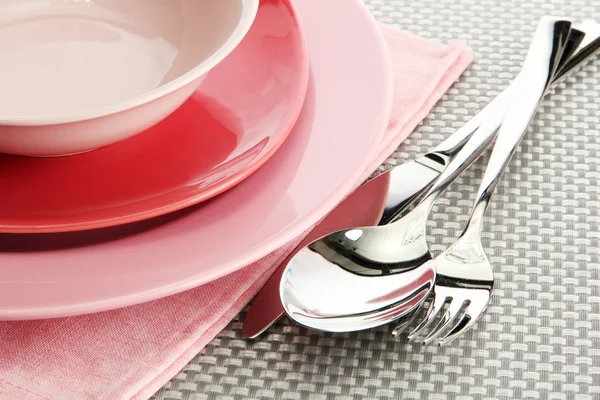 Розовые пустые тарелки с вилкой, ложкой и ножом на серой скатерти — стоковое фото